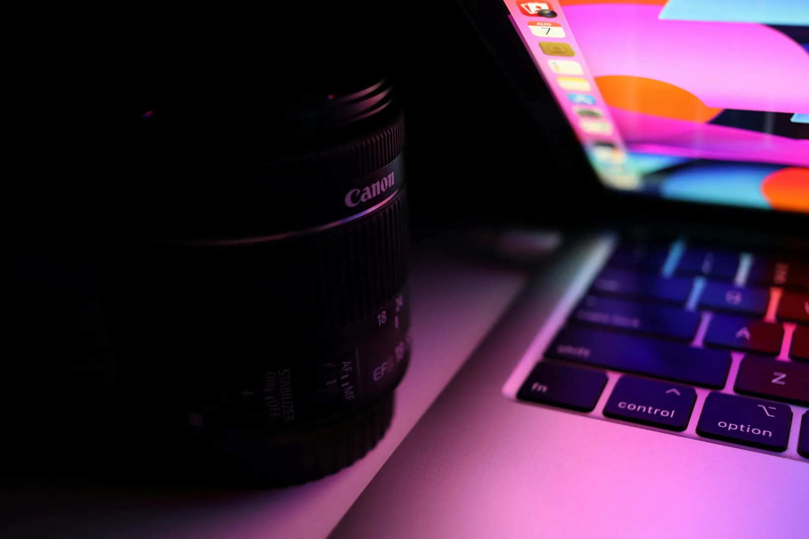 カラフルな光に照らされたCanonのカメラレンズとノートパソコン